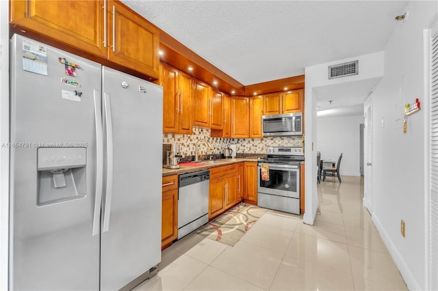900 NE 195th St Unit 317, Miami, FL 33179 - kitchen with stainless steel appliances, brown cabinets, tasteful backsplash, a sink, and light tile patterned floors
