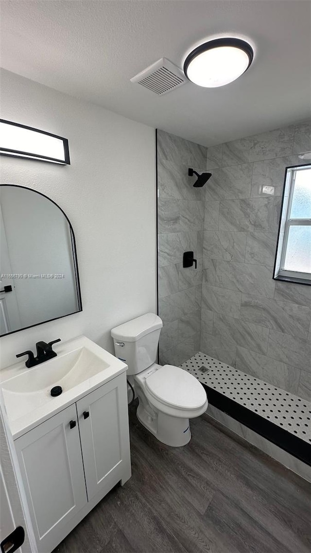 bathroom featuring toilet, tiled shower, vanity, and hardwood / wood-style floors