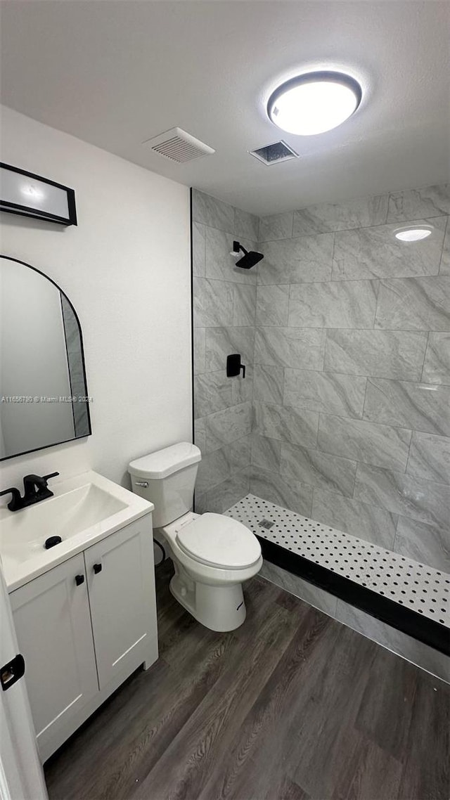 bathroom featuring vanity, hardwood / wood-style floors, toilet, and tiled shower