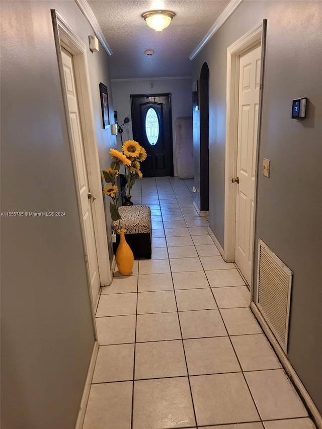 hallway with a textured ceiling, ornamental molding, and light tile patterned floors