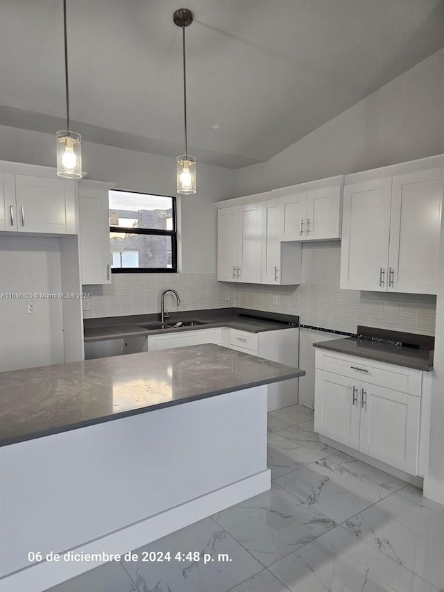 kitchen featuring tasteful backsplash, vaulted ceiling, sink, decorative light fixtures, and white cabinetry