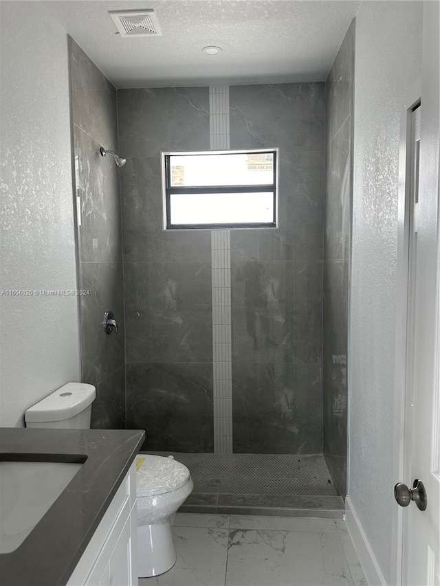 bathroom with tiled shower, vanity, and toilet