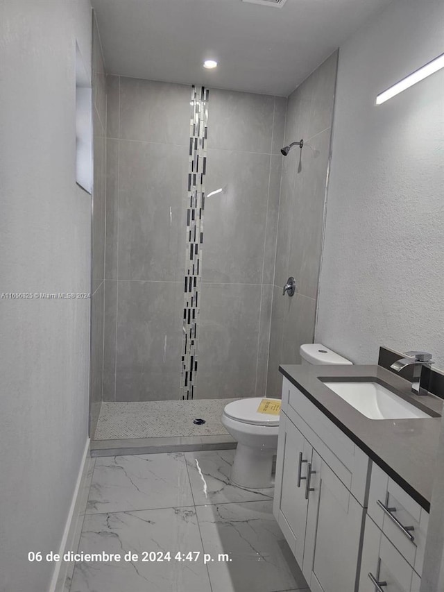 bathroom featuring a tile shower, vanity, and toilet