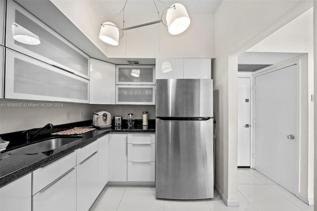 kitchen with white cabinets, light tile patterned flooring, stainless steel refrigerator, and sink