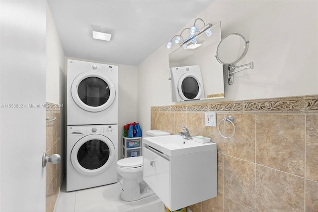 laundry area with stacked washer / dryer, tile walls, light tile patterned floors, and sink