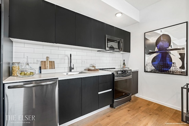 kitchen with light wood-type flooring, stainless steel appliances, sink, and decorative backsplash