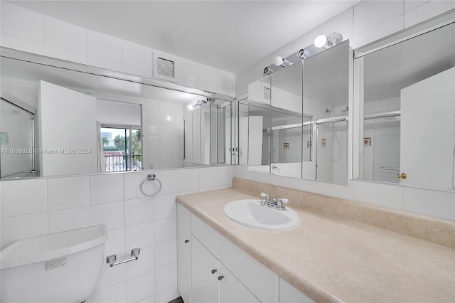 bathroom with vanity, toilet, tile walls, and a shower with door