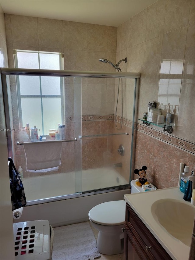 full bathroom with toilet, tile walls, bath / shower combo with glass door, vanity, and decorative backsplash