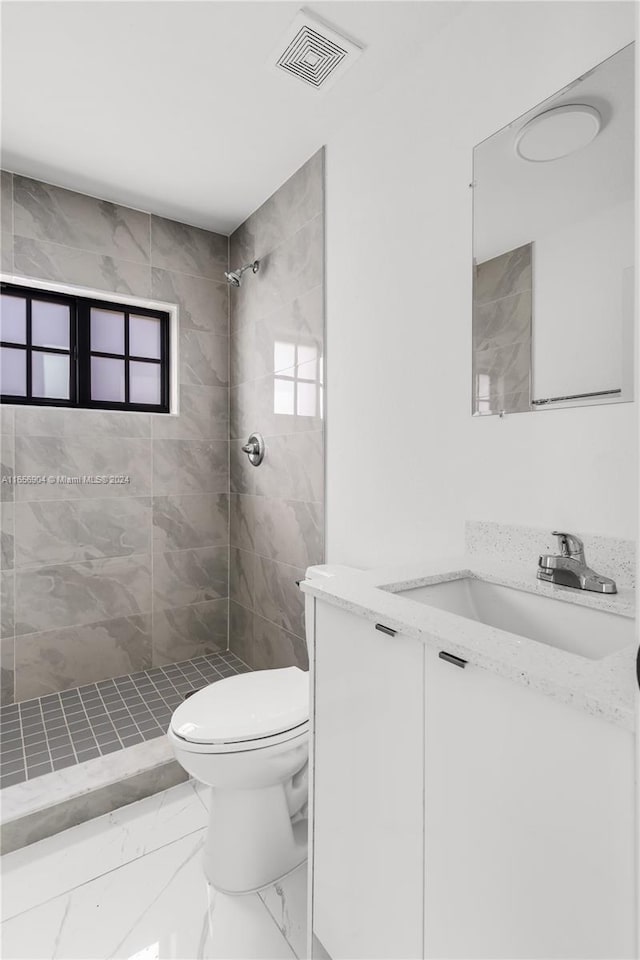 bathroom with a tile shower, vanity, and toilet