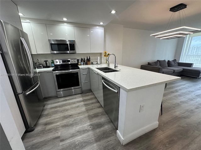 kitchen featuring decorative light fixtures, wood-type flooring, kitchen peninsula, sink, and appliances with stainless steel finishes