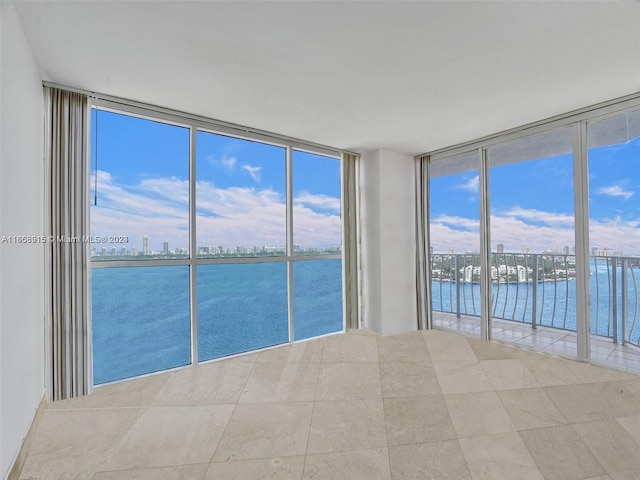 tiled empty room featuring a healthy amount of sunlight, floor to ceiling windows, and a water view