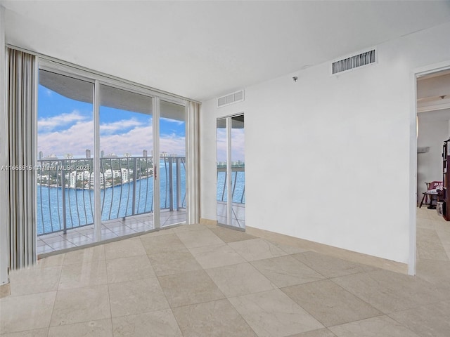 tiled empty room featuring a water view and floor to ceiling windows