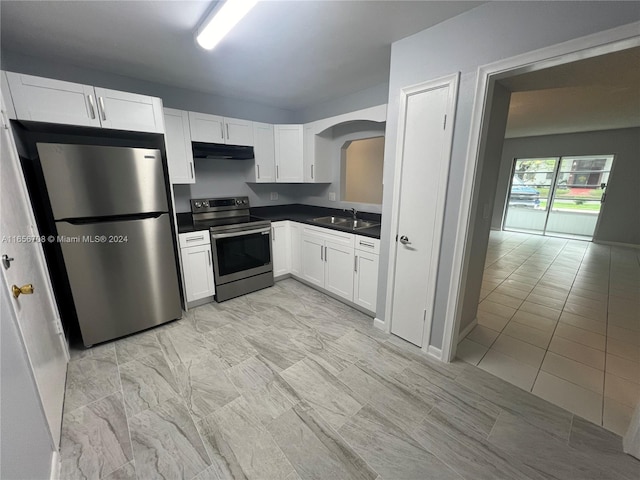 kitchen with dark countertops, under cabinet range hood, white cabinets, stainless steel appliances, and a sink