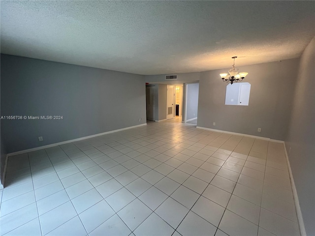 spare room featuring visible vents, a notable chandelier, a textured ceiling, light tile patterned floors, and baseboards