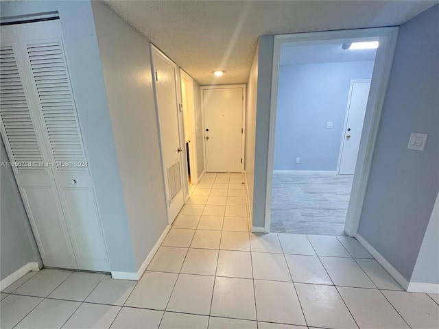 hallway with a textured ceiling and light tile patterned flooring