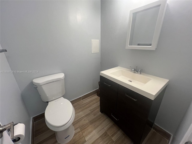 half bathroom featuring toilet, wood finished floors, and vanity