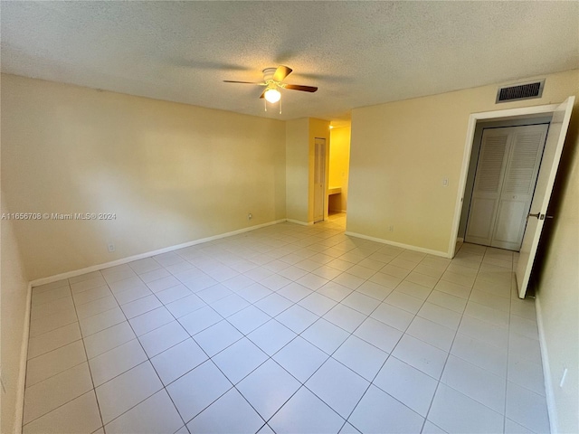 empty room featuring visible vents, baseboards, light tile patterned flooring, a textured ceiling, and a ceiling fan