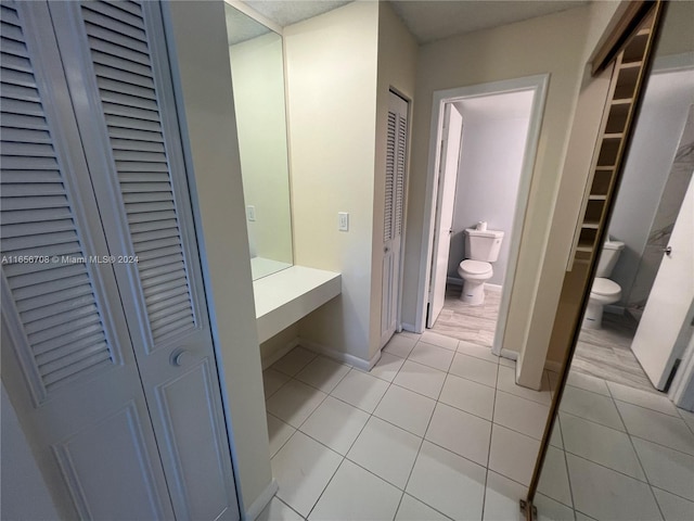 bathroom with tile patterned floors, toilet, baseboards, and a closet