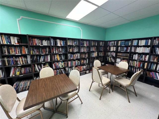 home office featuring tile patterned floors, a paneled ceiling, and wall of books