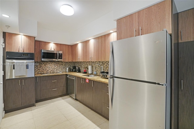 kitchen featuring stainless steel appliances, sink, light stone countertops, and decorative backsplash