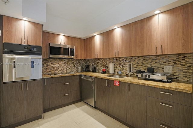 kitchen with light stone countertops, stainless steel appliances, tasteful backsplash, and sink