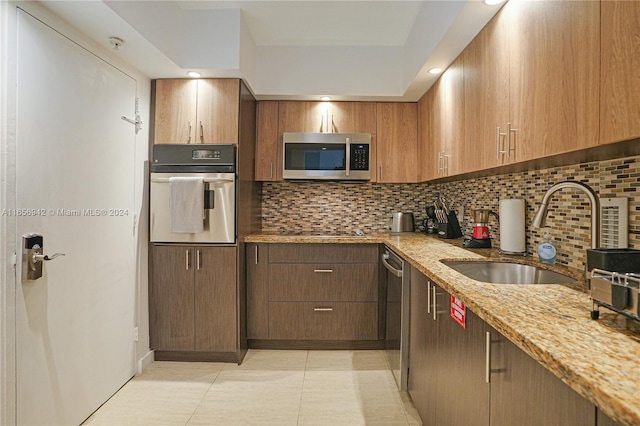 kitchen featuring appliances with stainless steel finishes, light stone counters, sink, and decorative backsplash