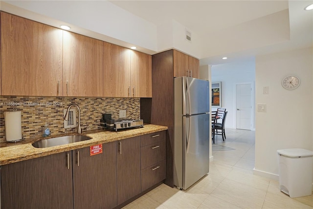 kitchen with light stone countertops, tasteful backsplash, stainless steel refrigerator, and sink