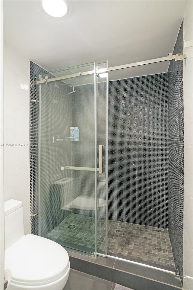 bathroom featuring a shower with door and toilet