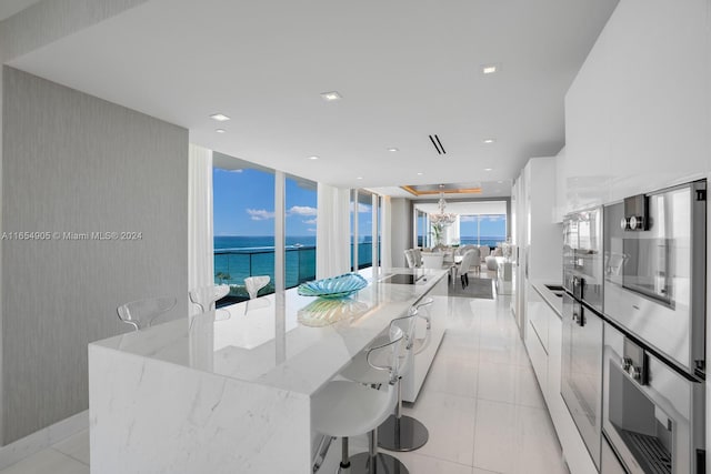 kitchen with a water view, light tile patterned floors, white cabinetry, and light stone countertops