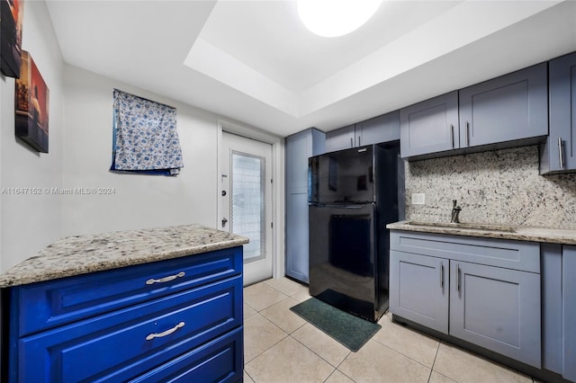 kitchen with a raised ceiling, light tile patterned floors, sink, light stone countertops, and black refrigerator