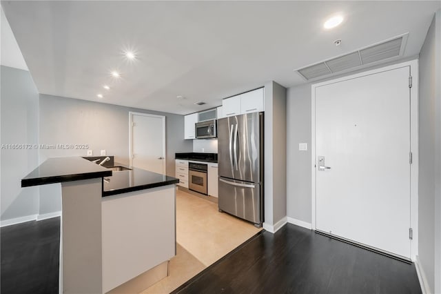 kitchen with sink, white cabinetry, kitchen peninsula, stainless steel appliances, and light hardwood / wood-style floors