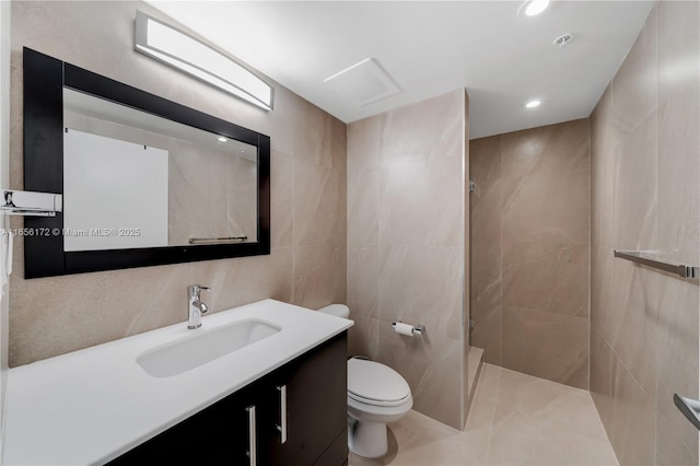 bathroom with vanity, toilet, tile walls, and a tile shower