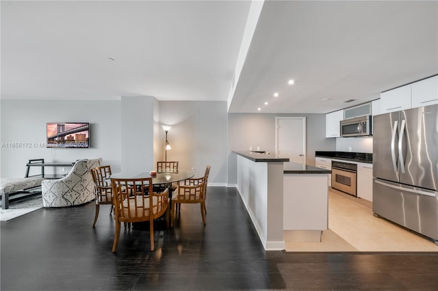 kitchen with appliances with stainless steel finishes, kitchen peninsula, white cabinets, and light hardwood / wood-style flooring