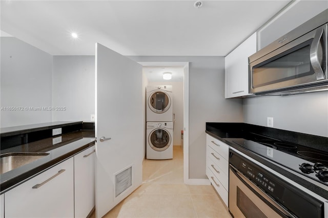 kitchen with stacked washing maching and dryer, light tile patterned flooring, sink, oven, and white cabinets