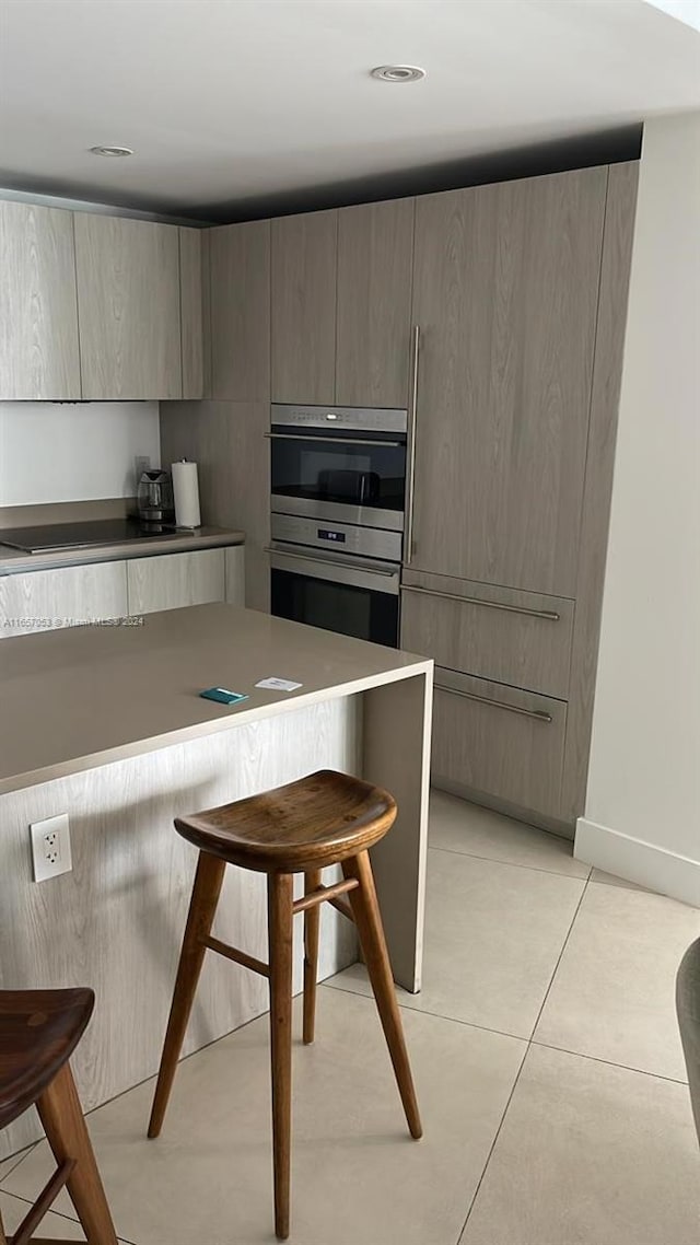 kitchen with double oven, a kitchen bar, light tile patterned floors, and black electric cooktop