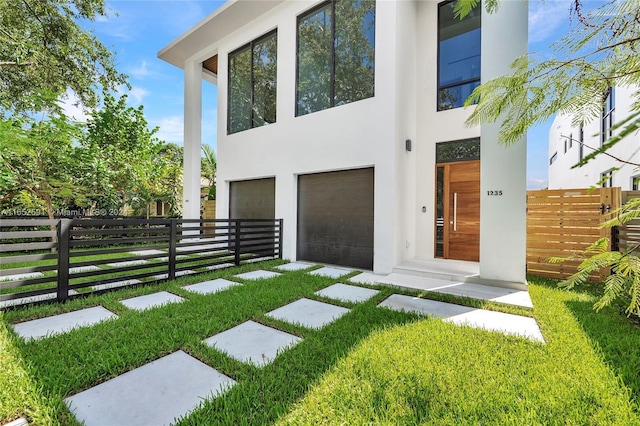 view of front facade featuring stucco siding, a front lawn, an attached garage, and fence