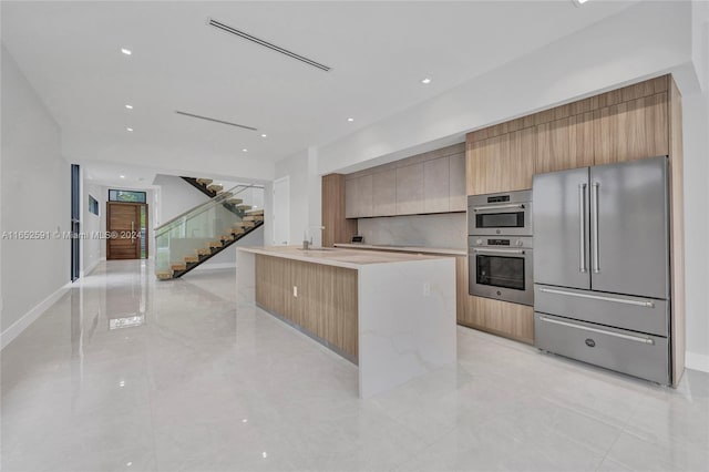 kitchen featuring an island with sink, sink, light brown cabinets, and appliances with stainless steel finishes