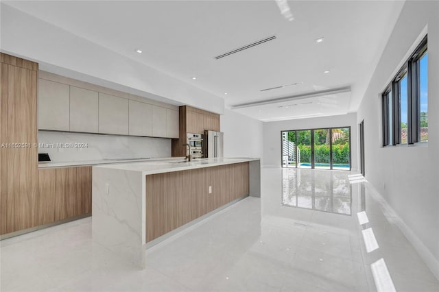 kitchen with stainless steel fridge, light stone countertops, a spacious island, light tile patterned floors, and decorative backsplash