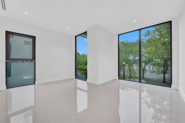 tiled empty room featuring floor to ceiling windows, recessed lighting, and baseboards