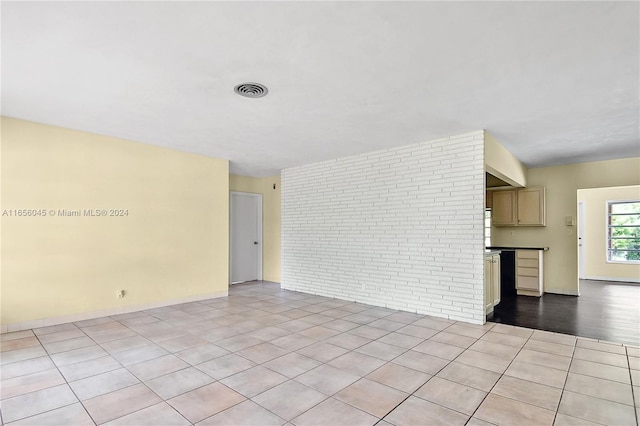 unfurnished living room featuring light tile patterned floors and brick wall