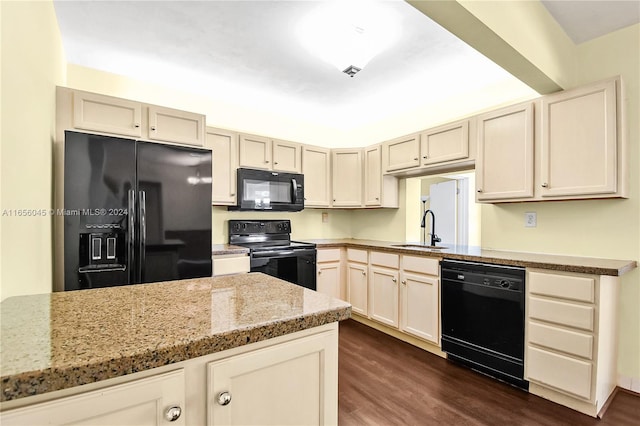 kitchen with light stone countertops, sink, dark hardwood / wood-style flooring, cream cabinetry, and black appliances