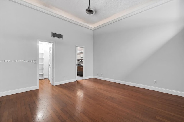 unfurnished bedroom with a high ceiling, a textured ceiling, a closet, dark wood-type flooring, and a walk in closet