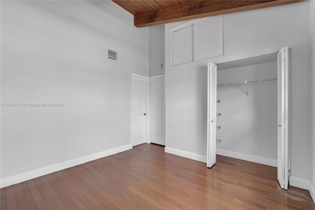 unfurnished bedroom with a closet, hardwood / wood-style flooring, beam ceiling, and a towering ceiling