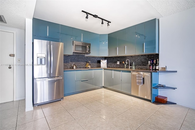 kitchen featuring blue cabinetry, appliances with stainless steel finishes, light tile patterned flooring, decorative backsplash, and a textured ceiling