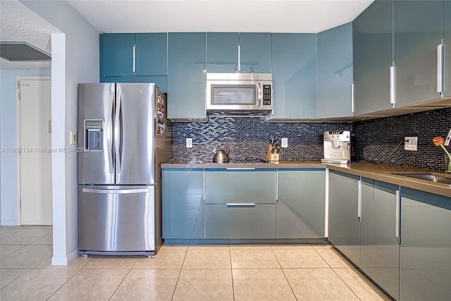 kitchen with sink, light tile patterned floors, appliances with stainless steel finishes, and decorative backsplash