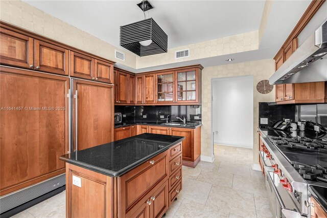 kitchen with decorative backsplash, dark stone counters, extractor fan, sink, and a center island