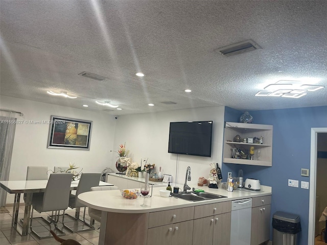 kitchen with light tile patterned floors, white dishwasher, sink, kitchen peninsula, and a textured ceiling