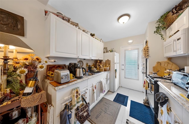 kitchen featuring white cabinets, light tile patterned flooring, and white appliances