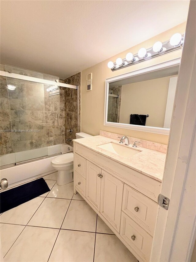 full bathroom with shower / bath combination with glass door, vanity, a textured ceiling, toilet, and tile patterned floors