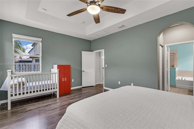 bedroom featuring dark wood-type flooring, a tray ceiling, ceiling fan, and connected bathroom